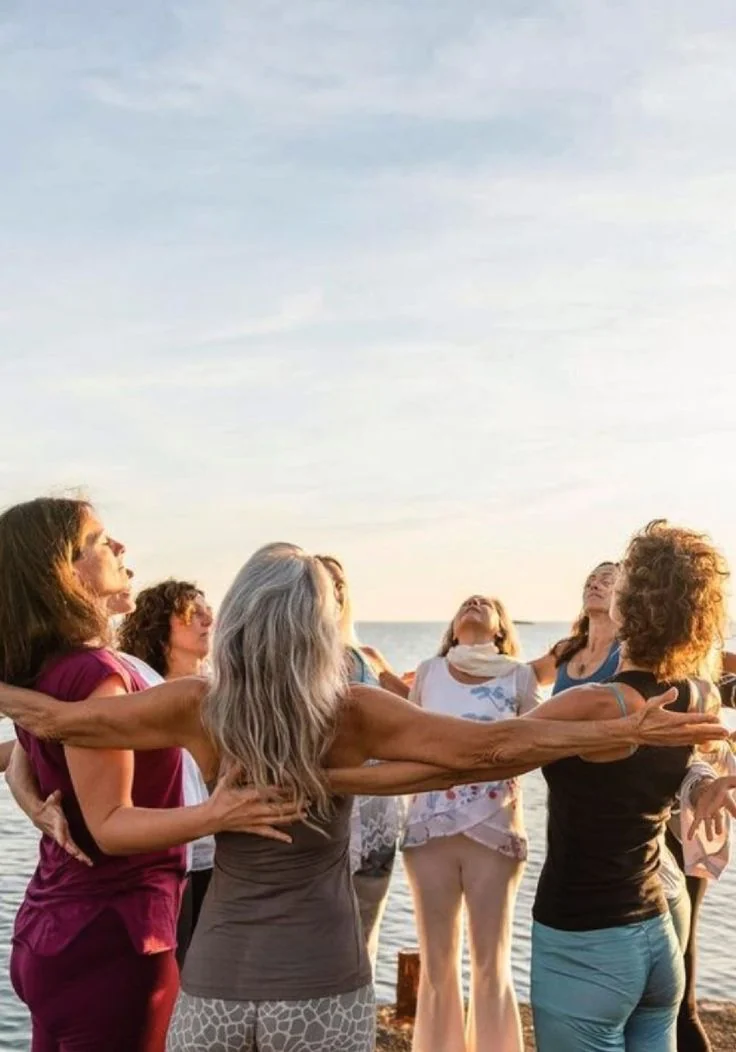 A circle of women of different ages on a beach, illustrating group experiences